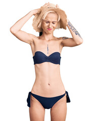 Fototapeta premium Young blonde woman with tattoo wearing bikini and summer hat suffering from headache desperate and stressed because pain and migraine. hands on head.