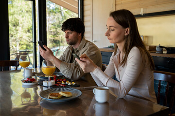 Fototapeta na wymiar Young family drinks coffee and looks at smartphones. A young couple using smartphones ignore each other. use mobile apps or check social networks online. steam and technological concept