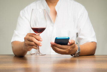 Close-up of hands holding a glass of red wine and a smartphone while sitting at the table.