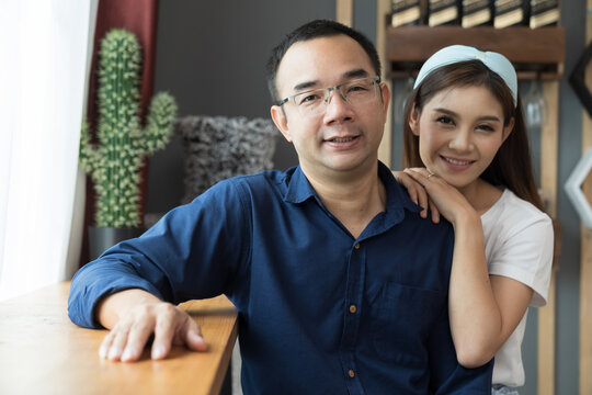 Happy smiling Asian couple sitting together and looking to camera at home