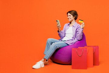 Young woman wear casual clothes purple shirt sit in bag chair near shopping paper package bags use...