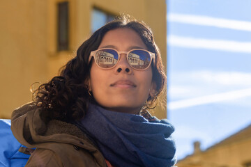 closeup of the face of a woman wearing sunglasses, with the reflection of an old medieval building