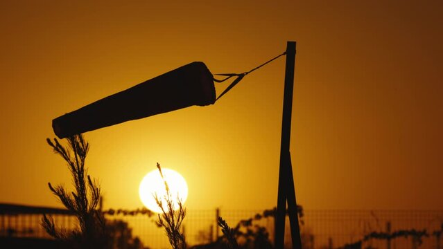Silhouette of wind sock at sunset sky. Wind sock in countryside at sunset. Wind indicator swinging at sunset transmits information about current wind direction helps to make accurate weather forecasts