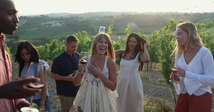 Multiracial people dancing at summer party inside vineyards - Adult friends having fun together drinking red wine  at coutryside resort - Travel, celebration and tasting event concept 
