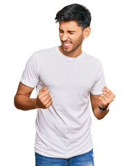 Young handsome man wearing casual white tshirt excited for success with arms raised and eyes closed celebrating victory smiling. winner concept.