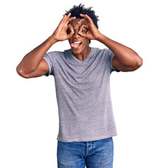 Fototapeta premium Handsome african american man with afro hair wearing casual clothes doing ok gesture like binoculars sticking tongue out, eyes looking through fingers. crazy expression.