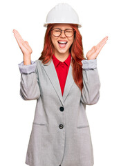 Young redhead woman wearing architect hardhat celebrating mad and crazy for success with arms raised and closed eyes screaming excited. winner concept
