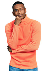 Young black man wearing orange turtleneck sweater serious face thinking about question with hand on chin, thoughtful about confusing idea