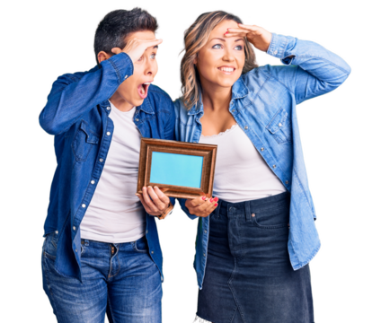 Couple of women holding empty frame very happy and smiling looking far away with hand over head. searching concept.