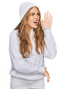 Young caucasian girl wearing wool sweater and winter cap shouting and screaming loud to side with hand on mouth. communication concept.