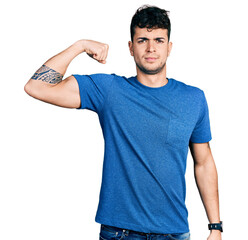 Young hispanic man wearing casual t shirt strong person showing arm muscle, confident and proud of power