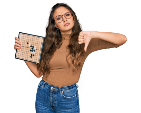 Young hispanic girl holding drauhgts with angry face, negative sign showing dislike with thumbs down, rejection concept