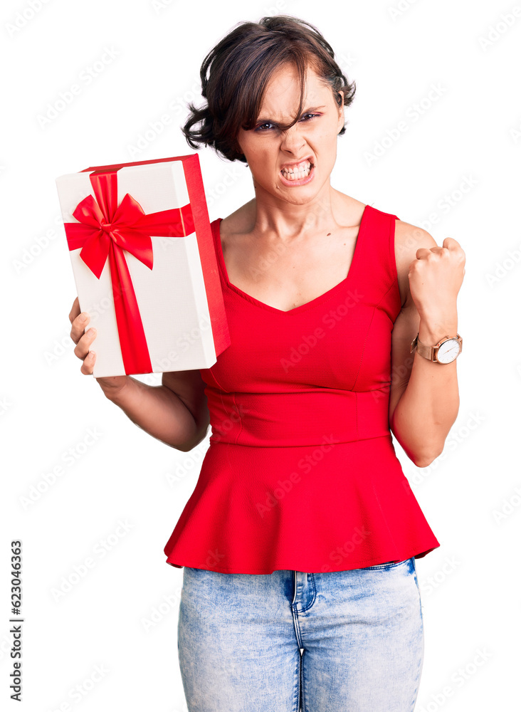 Poster beautiful young woman with short hair holding gift annoyed and frustrated shouting with anger, yelli