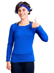 Beautiful young woman with short hair wearing training workout clothes doing happy thumbs up gesture with hand. approving expression looking at the camera showing success.