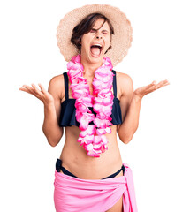 Beautiful young woman with short hair wearing bikini and hawaiian lei celebrating mad and crazy for...