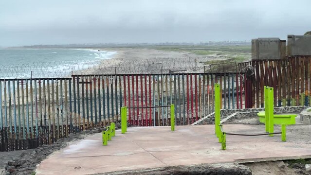 Camera pans along the border wall that separates the United States and Mexico. On the other side, in the distance, we see san Diego. Filmed on an overcast day in Playas de Tijuana (Mexico).