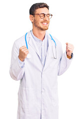 Fototapeta premium Handsome young man with bear wearing doctor uniform excited for success with arms raised and eyes closed celebrating victory smiling. winner concept.