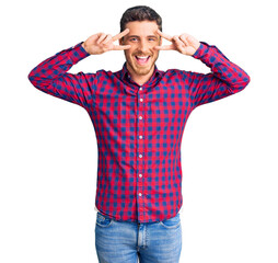 Handsome young man with bear wearing casual shirt doing peace symbol with fingers over face, smiling cheerful showing victory