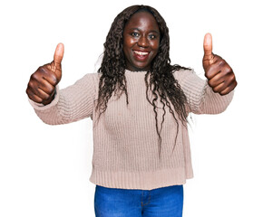 Young african woman wearing wool winter sweater approving doing positive gesture with hand, thumbs up smiling and happy for success. winner gesture.