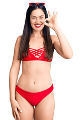 Young beautiful caucasian woman wearing bikini smiling positive doing ok sign with hand and fingers. successful expression.