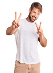 Young caucasian man wearing casual white tshirt smiling looking to the camera showing fingers doing victory sign. number two.