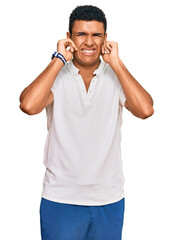 Fototapeta premium Young arab man wearing casual clothes covering ears with fingers with annoyed expression for the noise of loud music. deaf concept.