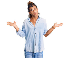 Young hispanic man wearing summer style clueless and confused expression with arms and hands...