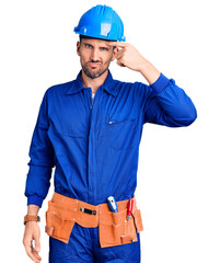 Young handsome man wearing worker uniform and hardhat covering eyes with hand, looking serious and sad. sightless, hiding and rejection concept