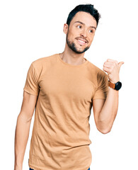 Hispanic man with beard wearing casual t shirt smiling with happy face looking and pointing to the side with thumb up.