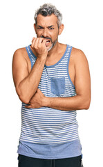 Middle age grey-haired man wearing casual style with sleeveless shirt looking stressed and nervous with hands on mouth biting nails. anxiety problem.