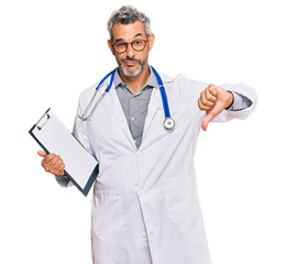 Middle age grey-haired man wearing doctor stethoscope holding clipboard with angry face, negative...