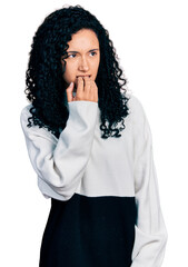 Fototapeta na wymiar Young hispanic woman with curly hair wearing casual sweater looking stressed and nervous with hands on mouth biting nails. anxiety problem.
