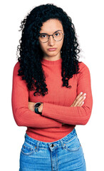 Young hispanic woman with curly hair wearing glasses skeptic and nervous, disapproving expression...