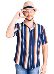 Young handsome caucasian man wearing summer hat smiling and confident gesturing with hand doing small size sign with fingers looking and the camera. measure concept.