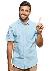 Handsome hispanic man wearing casual clothes showing and pointing up with finger number one while smiling confident and happy.