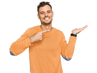 Young hispanic man wearing casual clothes amazed and smiling to the camera while presenting with hand and pointing with finger.