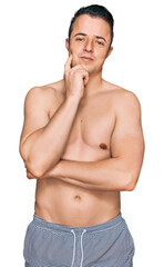 Fototapeta premium Handsome young man wearing swimwear shirtless with hand on chin thinking about question, pensive expression. smiling and thoughtful face. doubt concept.