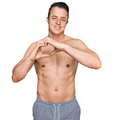 Fototapeta premium Handsome young man wearing swimwear shirtless smiling in love doing heart symbol shape with hands. romantic concept.