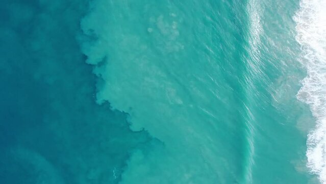 Top view of the turquoise ocean water and waves. The waves raise the sand, changing the shade of the water to dark blue. Shadows from clouds float on the sea. Water gradient. Phuket, Karon Beach