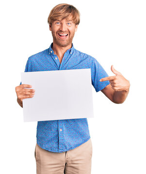 Handsome caucasian man with beard holding sale poster smiling happy pointing with hand and finger