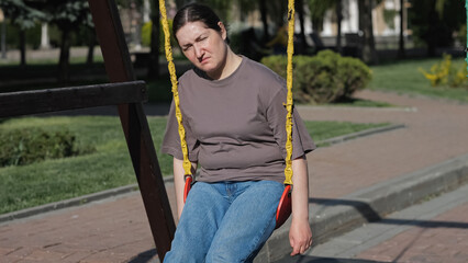 Upset depressed woman swinging on playground in city park illuminated by bright sunlight. Lady sits having bad thoughts about life