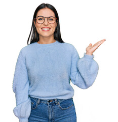 Young hispanic woman wearing casual clothes and glasses smiling cheerful presenting and pointing...