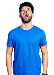 Young arab man with beard wearing casual blue t shirt angry and mad screaming frustrated and furious, shouting with anger. rage and aggressive concept.