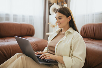 Young woman freelancer working online using laptop, sitting in a cozy living room