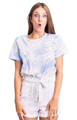 Young beautiful blonde woman wearing tye die tshirt scared and amazed with open mouth for surprise,...