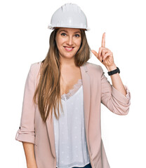 Young blonde woman wearing architect hardhat pointing finger up with successful idea. exited and happy. number one.