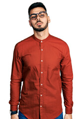 Young hispanic man with beard wearing business shirt and glasses relaxed with serious expression on face. simple and natural looking at the camera.