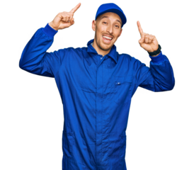 Bald man with beard wearing builder jumpsuit uniform smiling amazed and surprised and pointing up with fingers and raised arms.