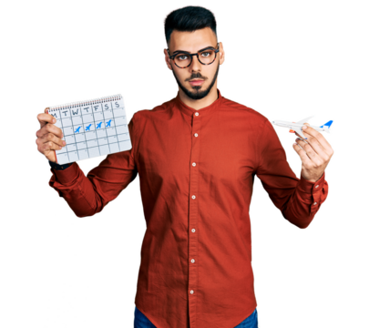 Young hispanic man with beard holding plane toy and travel calendar relaxed with serious expression on face. simple and natural looking at the camera.