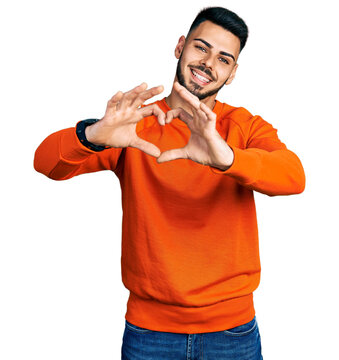 Young hispanic man with beard wearing casual orange sweater smiling in love doing heart symbol shape with hands. romantic concept.